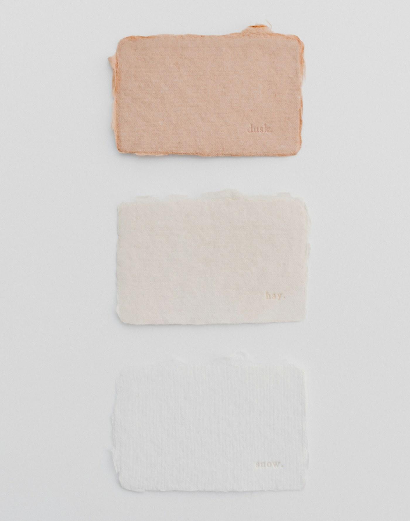 Three textured paper swatches — peach, cream and white — on a white surface